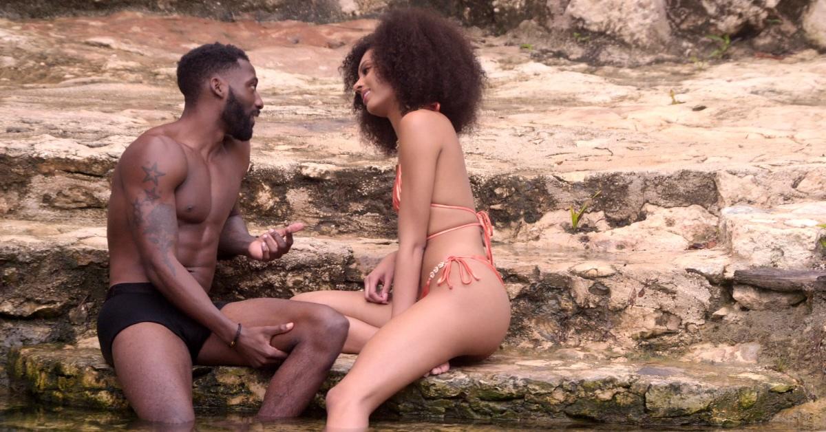 Kaz, in black briefs, and Christine, in a skimpy orange bikini, sit on a rock and talk in Season 2, Episode 8 of 'Perfect Match.'