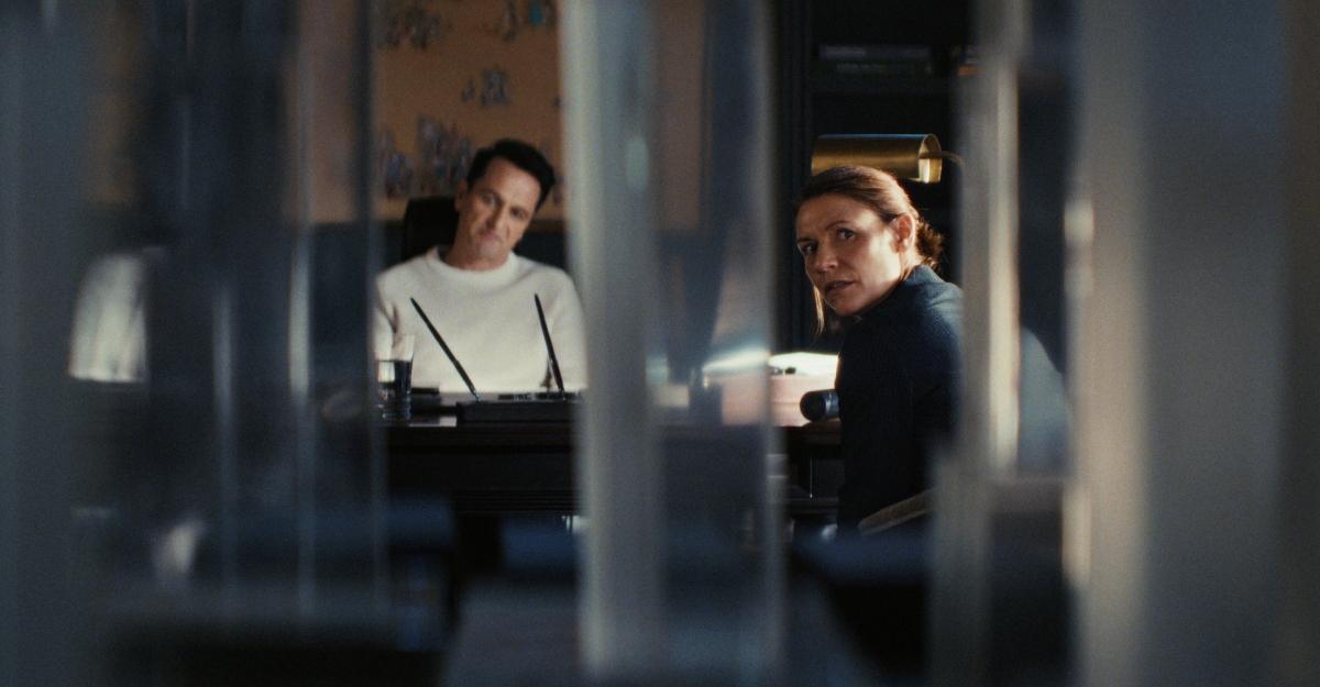 Nile and Aggie sit in an office as Aggie looks over her shoulder