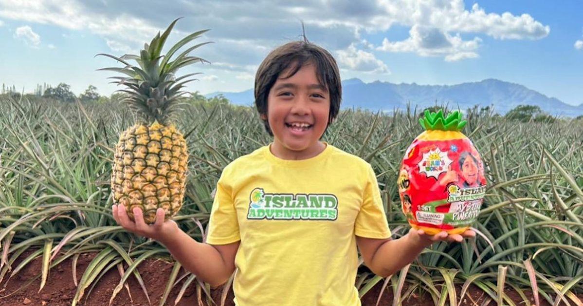 Ryan holding a pineapple and his trademark egg while wearing yellow shirt