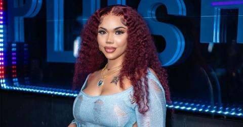 Renni Rucci smirks in front of glowing blue letters wearing a blue spiderweb dress.