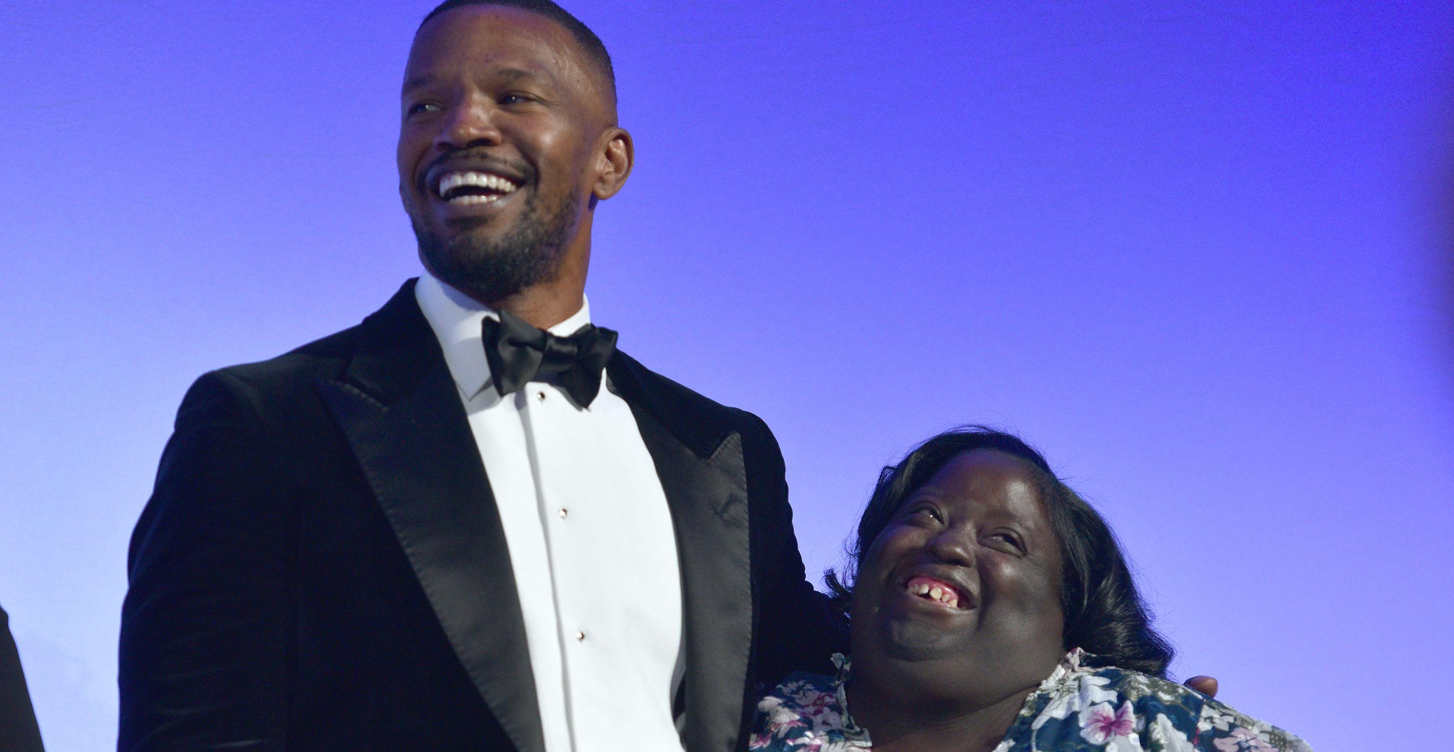 Jamie Foxx smiles with his arm around his sister, while wearing a tuxedo.