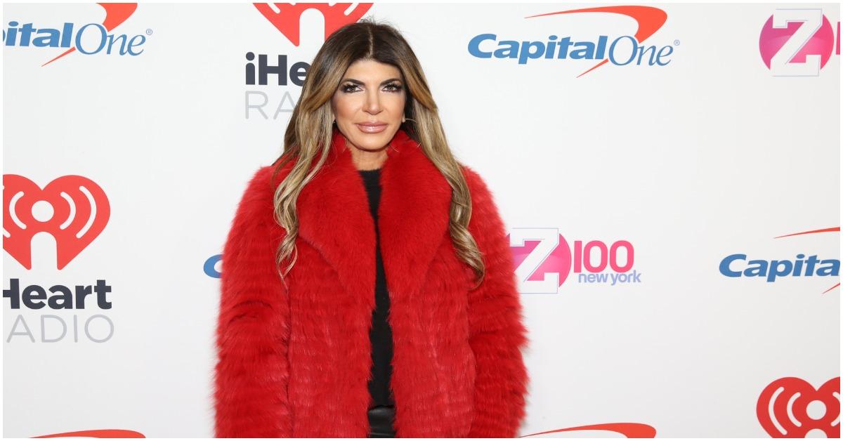 Teresa Giudice posing in a red, furry coat at an event.