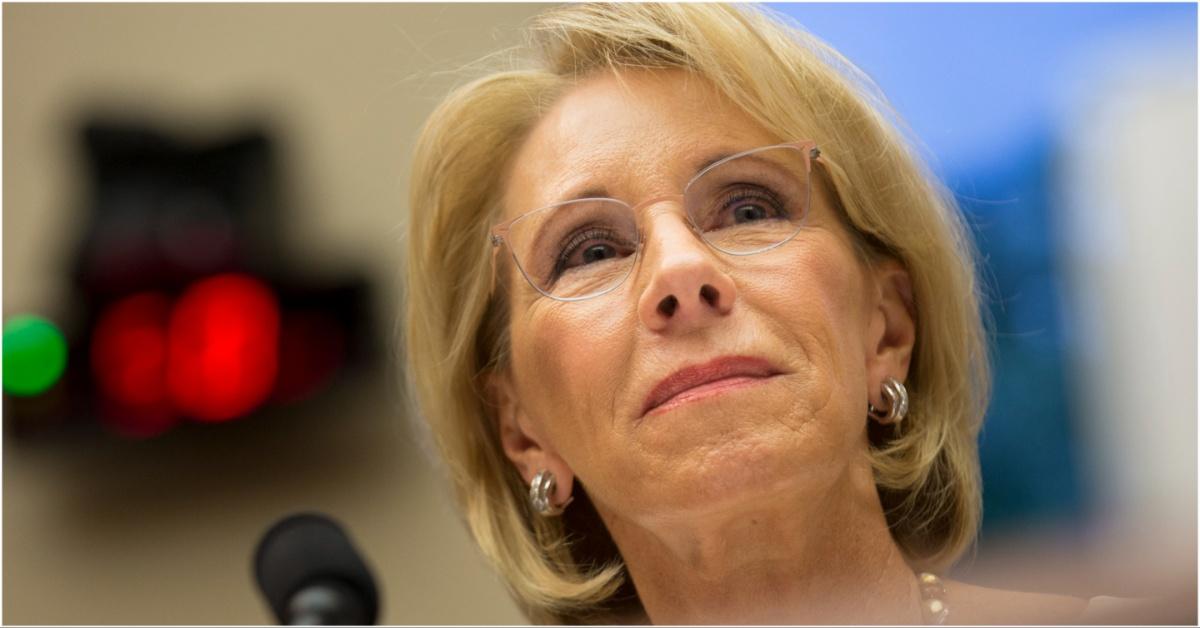 Betsy DeVos smiling next to a microphone