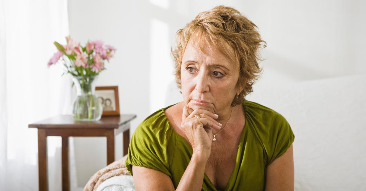 A sad woman sits on her couch and thinks about her life.