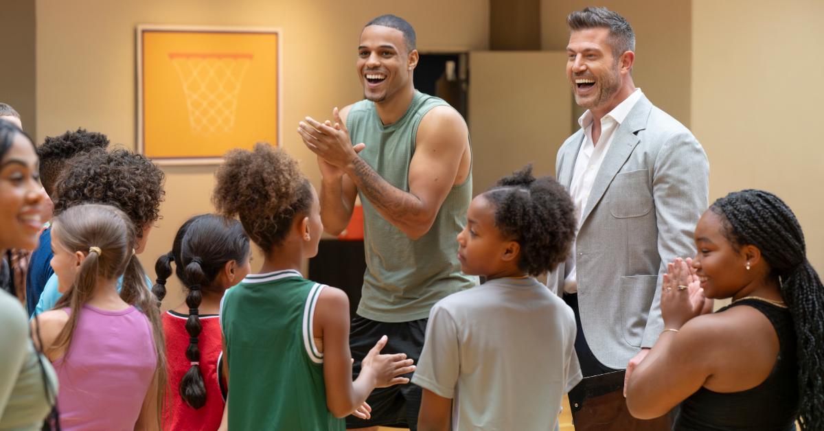 Grant Ellis and Jesse Palmer chat with a group of kids on a basketball court on 'The Bachelor.'