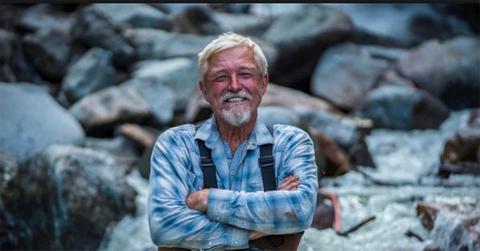 'Dakota' Fred Hurt in overalls standing with his arms crossed.