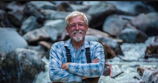 'Dakota' Fred Hurt in overalls standing with his arms crossed.