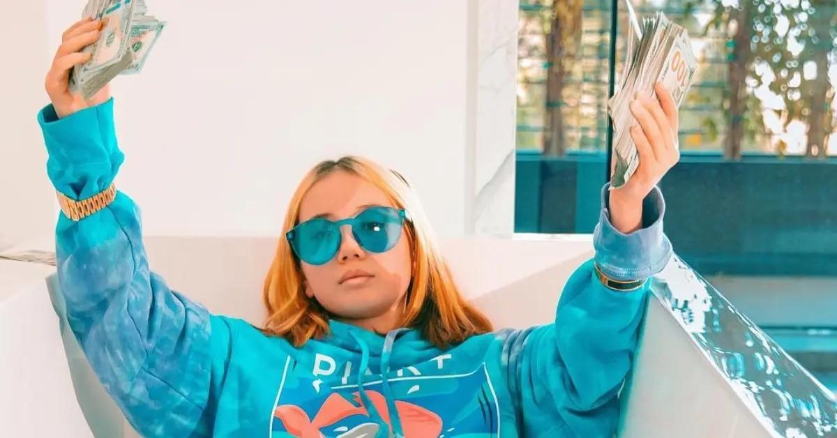 Lil Tay holding money and wearing a bright blue hoodie and sunglasses.