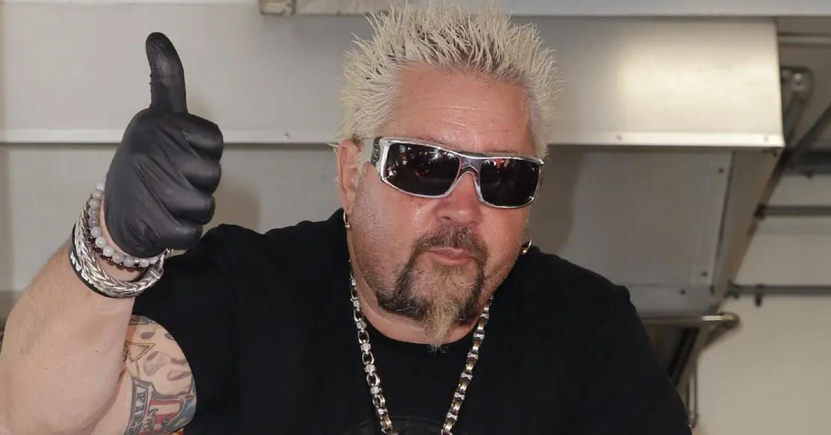 Guy Fieri, in a black shirt and sunglasses, gives a thumbs up 