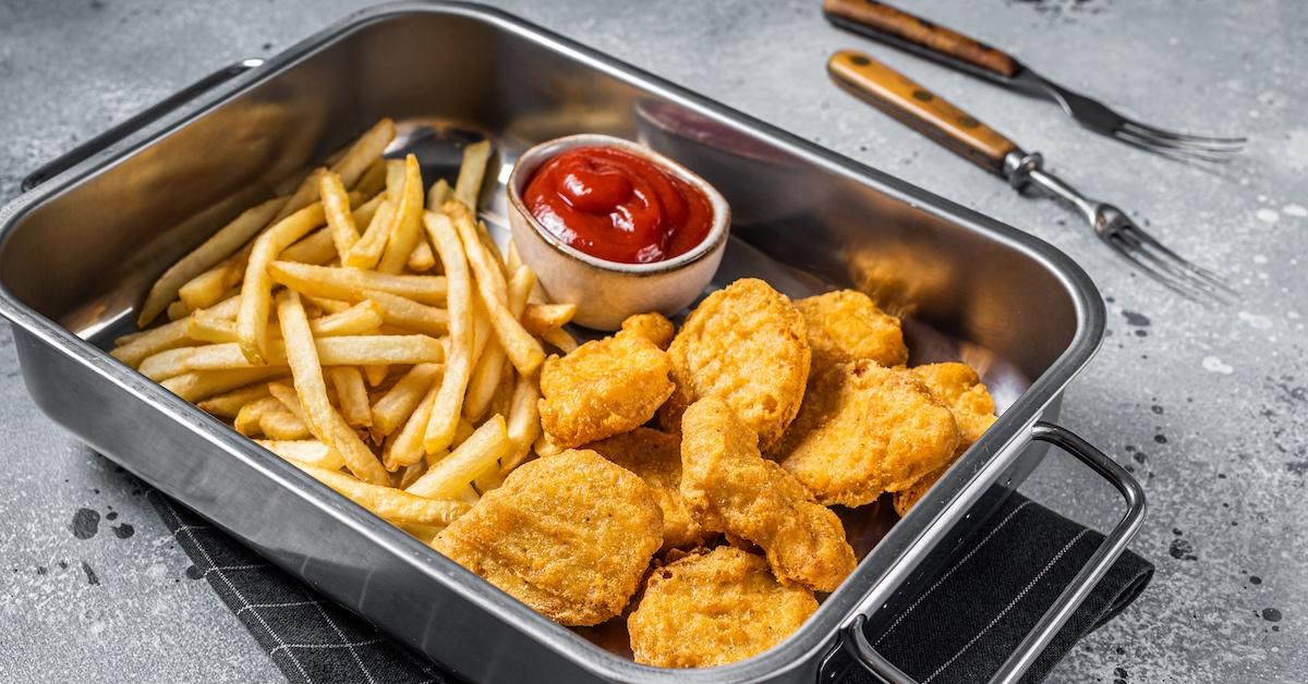 A metal container with french fries and chicken nuggets with ketchup