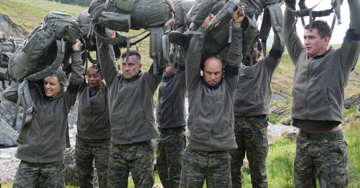 Worlds Toughest Test cast members hold their bags above their heads in camo