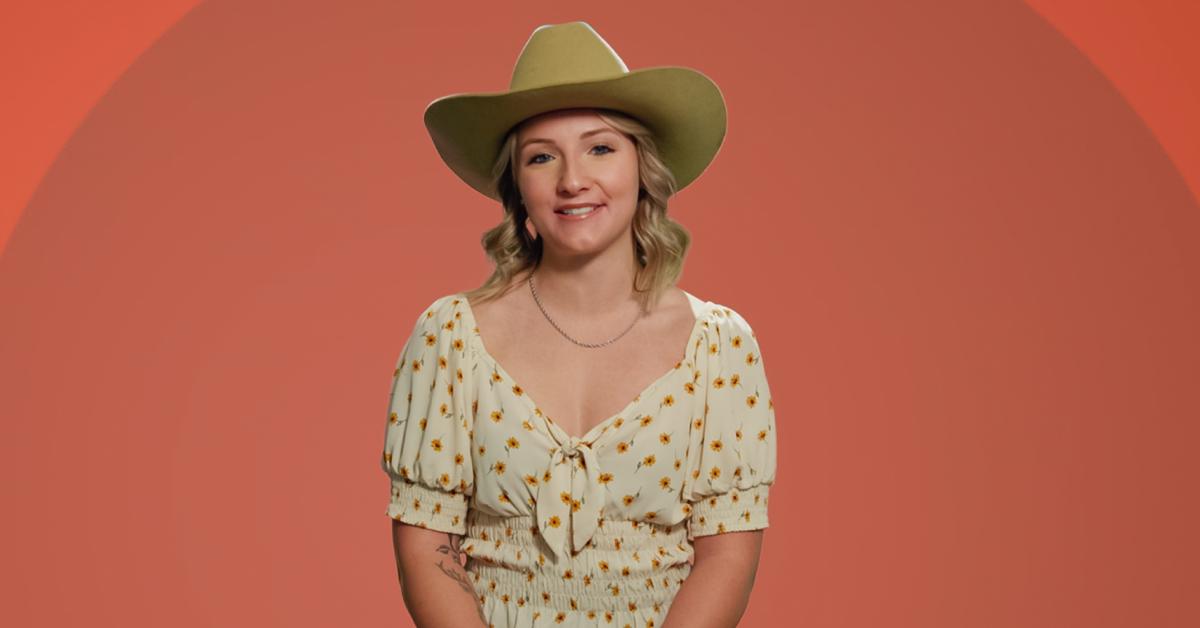 Autumn wears a floral print dress and a tan-colored cowboy hat while posing in front of an orange background for 'The Circle' Season 6.