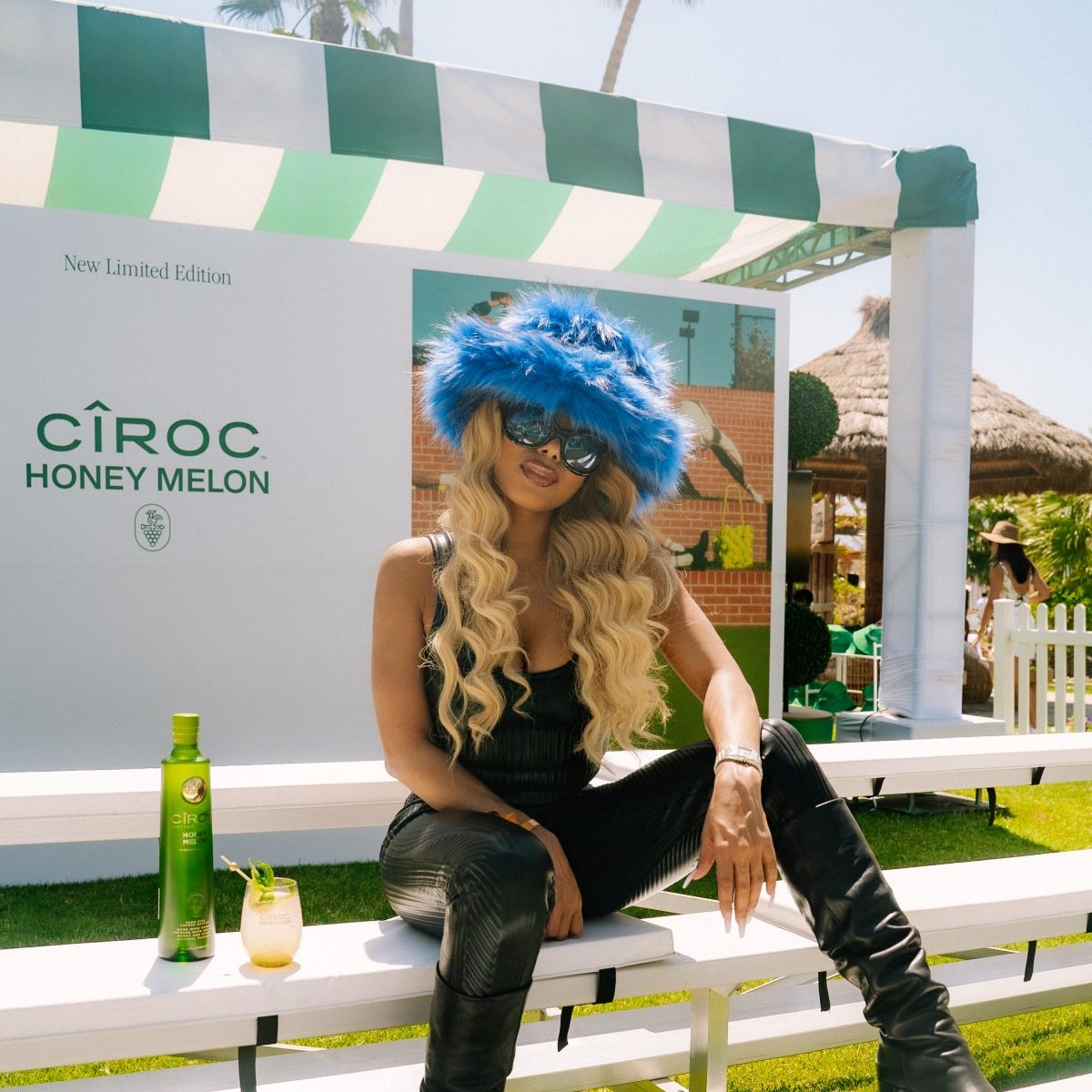 Lady London wears a blue fuzzy hat and shades sitting next to Circo's Honeydew Melon vodka.