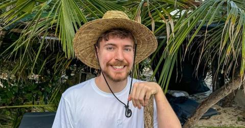MrBeast smiling while wearing a floppy hat in front of palm trees