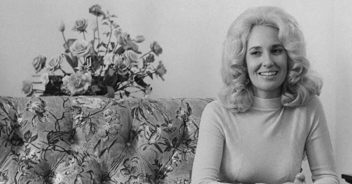 Tammy Wynette smiles next to a bouquet of roses and sits on a floral print couch.