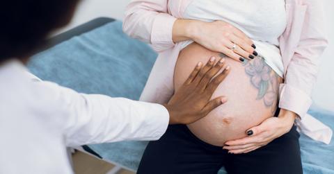 Health practitioner places a hand on the pregnant belly of a woman with a visible tattoo.