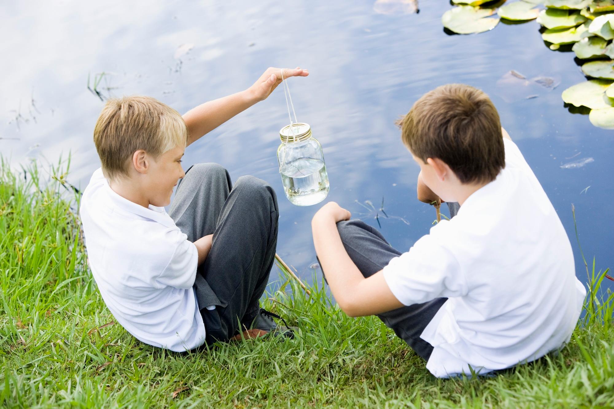 two boys sitting outside by a lake