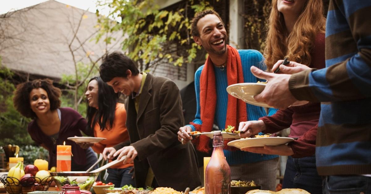 A group of friends laughing as they add food to their plates.