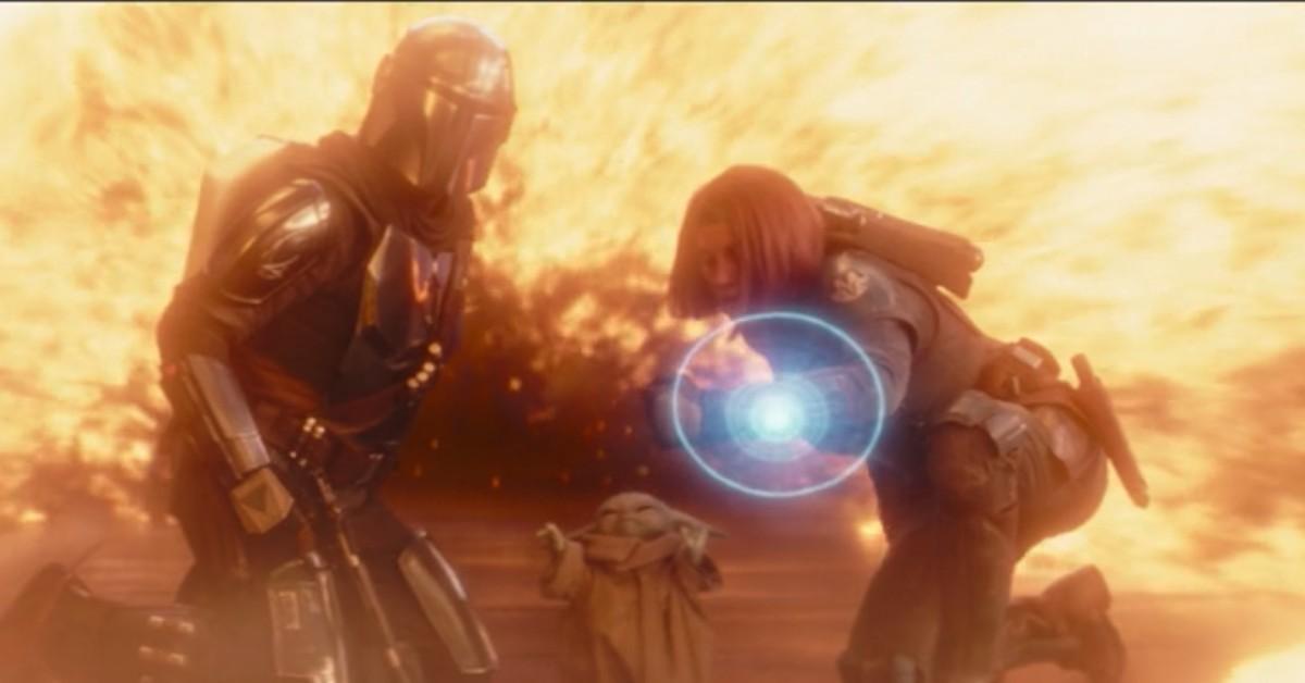 (L-R) Din Djarin (Pedro Pascal), Grogu, and Bo-Katan (Katee Sackhoff) are surrounded by flames 