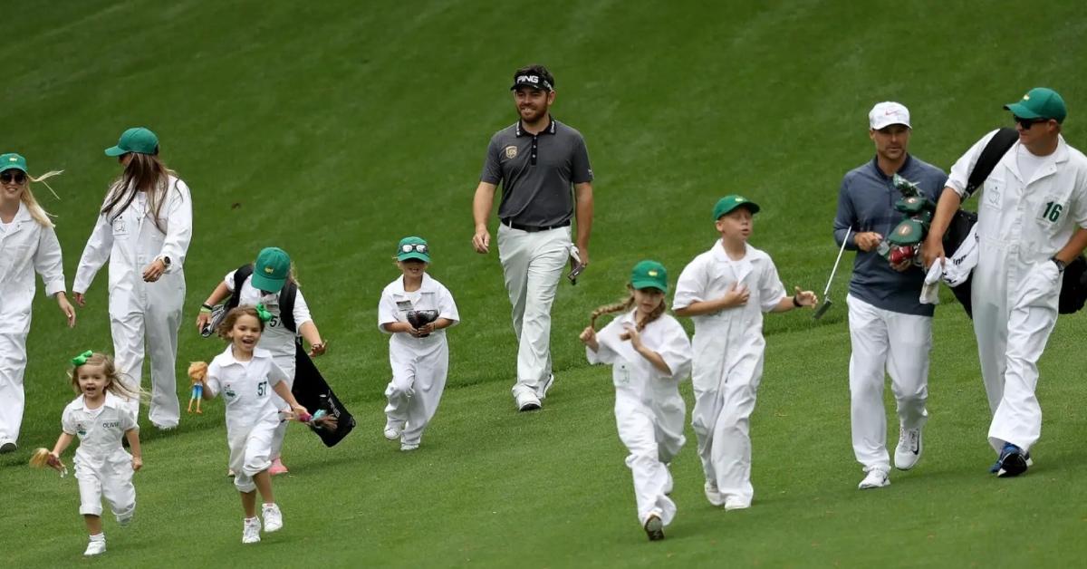 A golfer and gold caddies wearing white jumpsuits walking on the golf course.