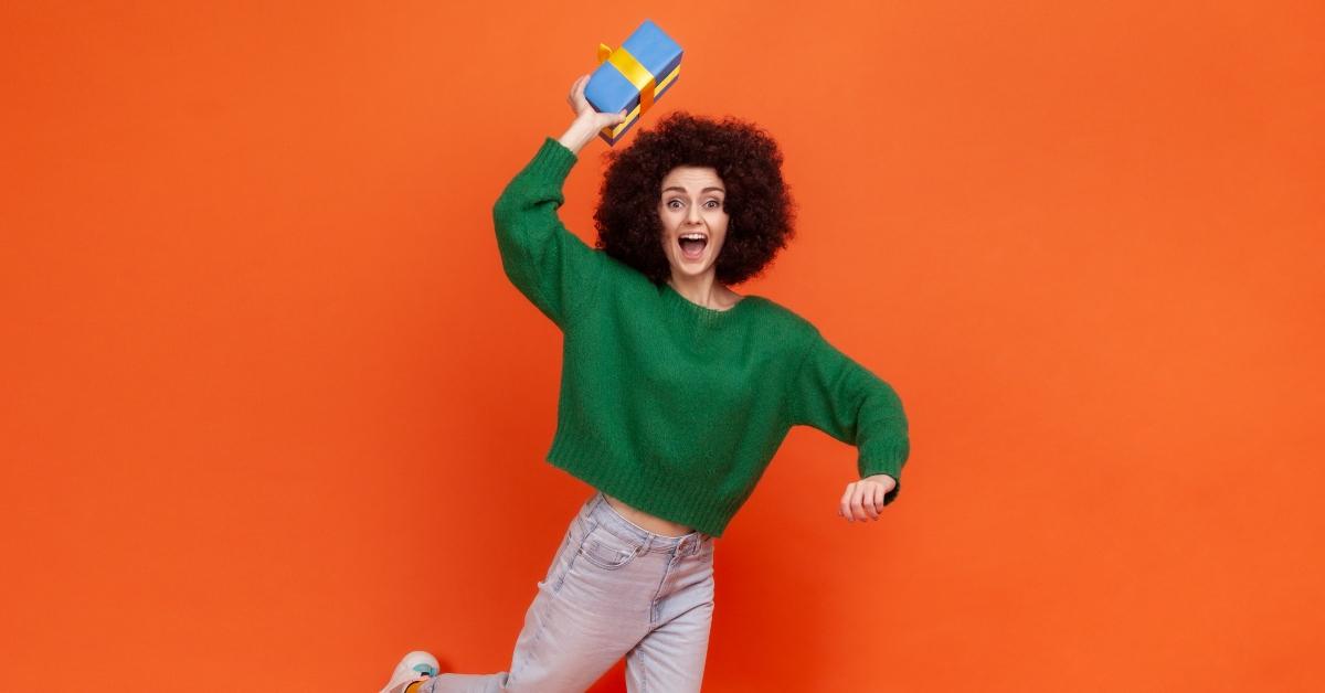 Woman with a green sweater against an orange background holding a blue gift box.