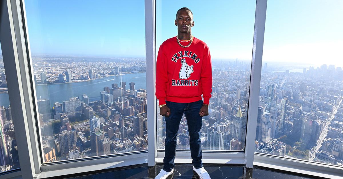 Israel Adesanya standing in a tall building looking out over a skyline. 