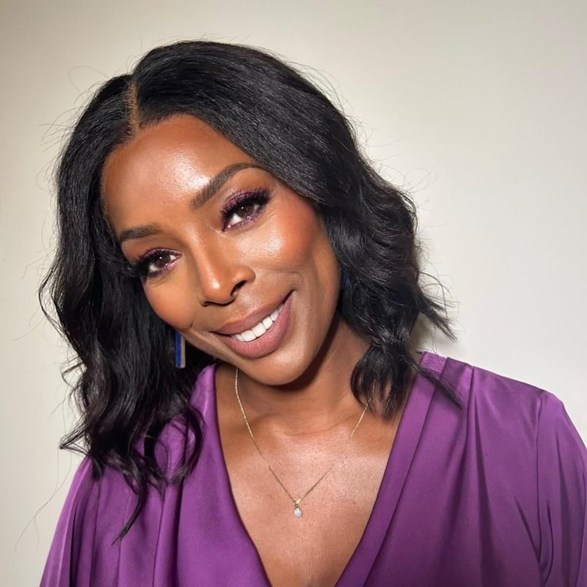 Tasha Smith smiling wearing a purple blouse with purple eyeshadow.