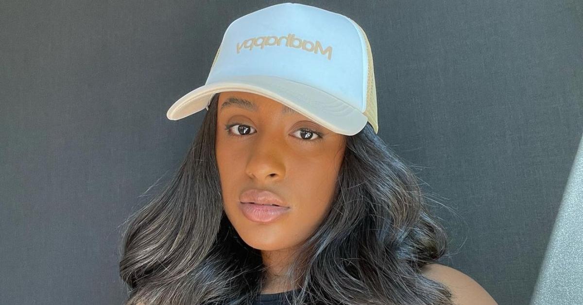 TikTok influencer Bria Jones posing in front of a black background wearing a white and yellow hat.