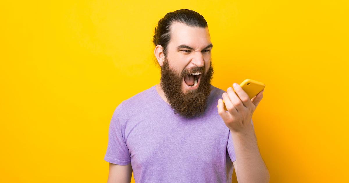 man with beard and purple shirt angry at iPhone