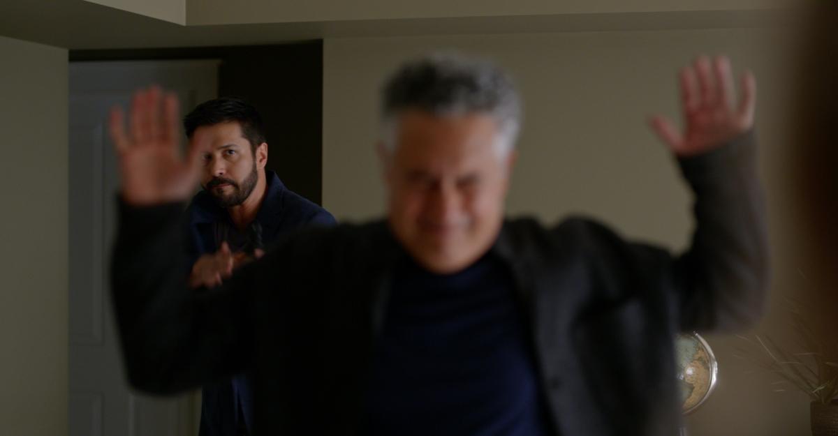 Grant raises his arms over his head in surrender as Mike points a gun at him.