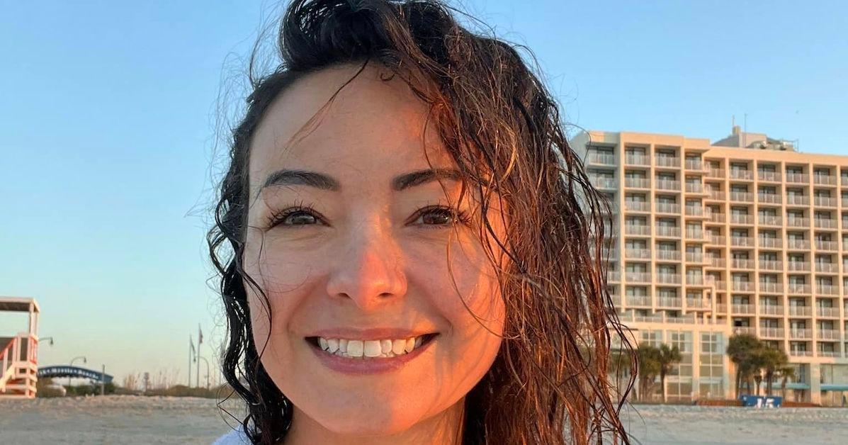 Mica Miller on the beach smiling with buildings behind her