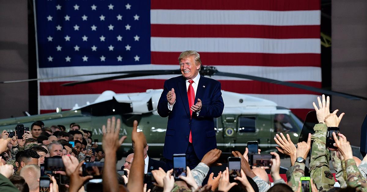 Donald Trump greeting troops in front of a flag and a helicopter. 