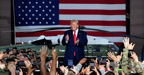 Donald Trump greeting troops in front of a flag and a helicopter.