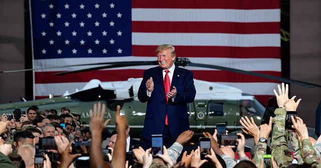 Donald Trump greeting troops in front of a flag and a helicopter.