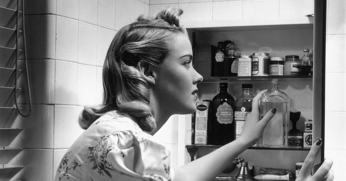 Woman reaches for bottle in medicine cabinet - stock photo, c. 1950s