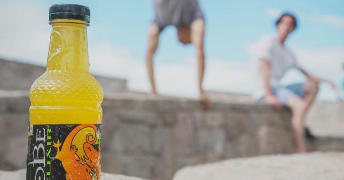 An orange SoBe sitting on the ground with two men in the background