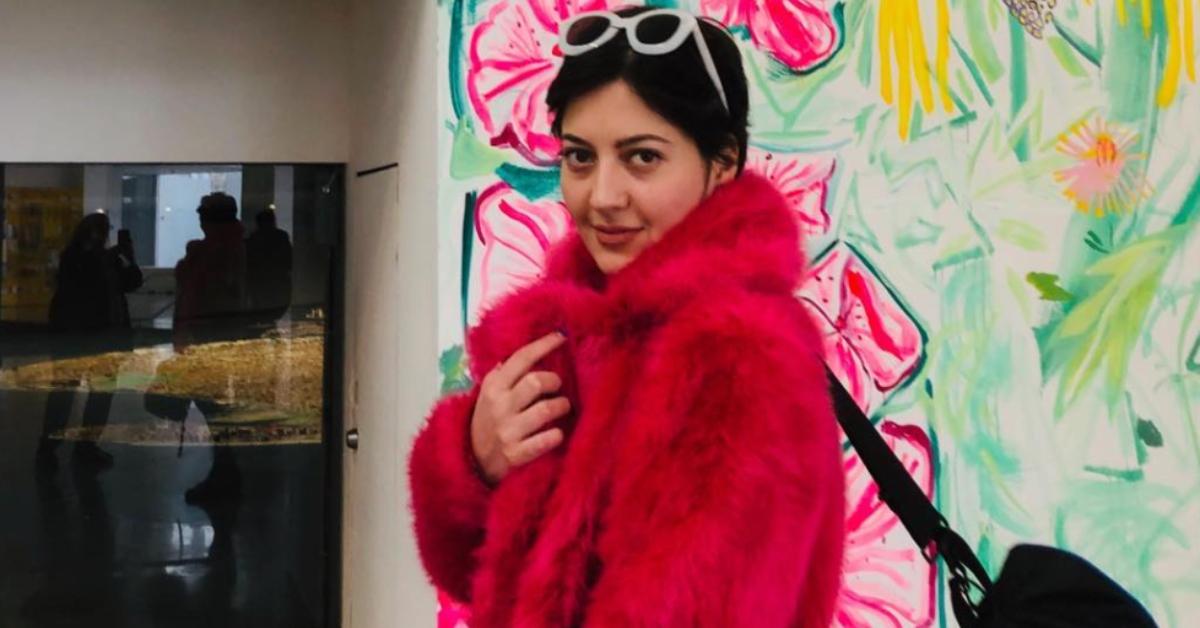 Sabina Rosas stands in an art gallery wearing a red coat