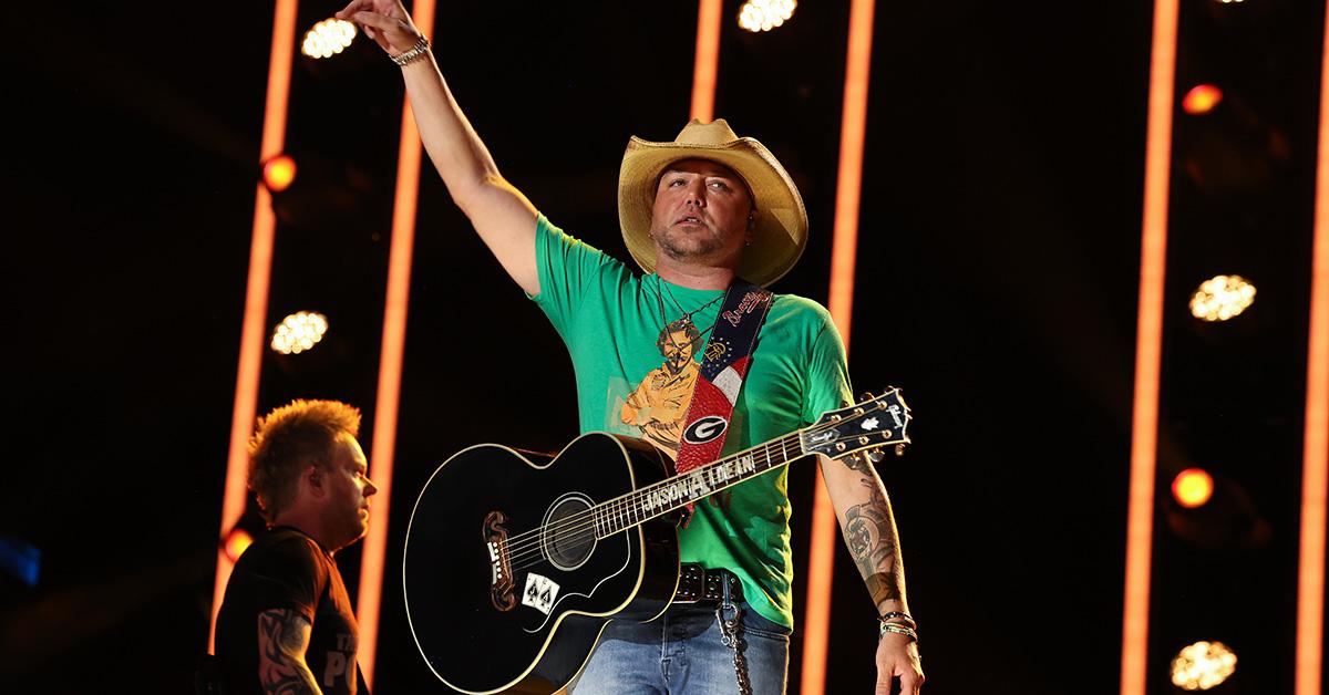 Jason Aldean in a green shirt with a guitar over his shoulder.