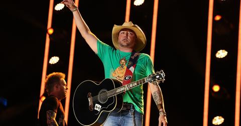 Jason Aldean in a green shirt with a guitar over his shoulder.