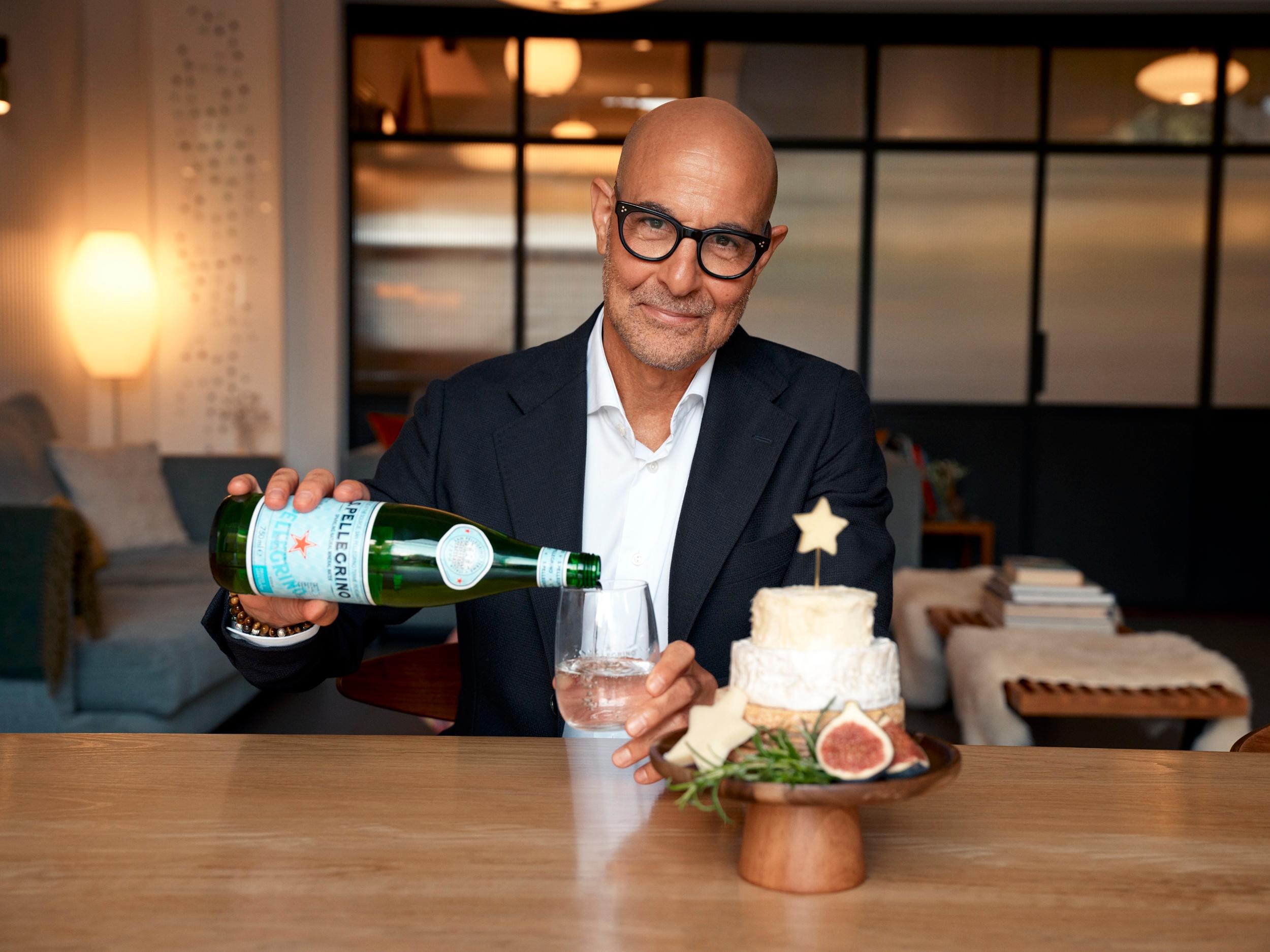 Stanley Tucci pouring S.Pellegrino in a glass right next to the "S.Pellegrino & Stanley Tucci's Holiday Cheese 'Cake'"