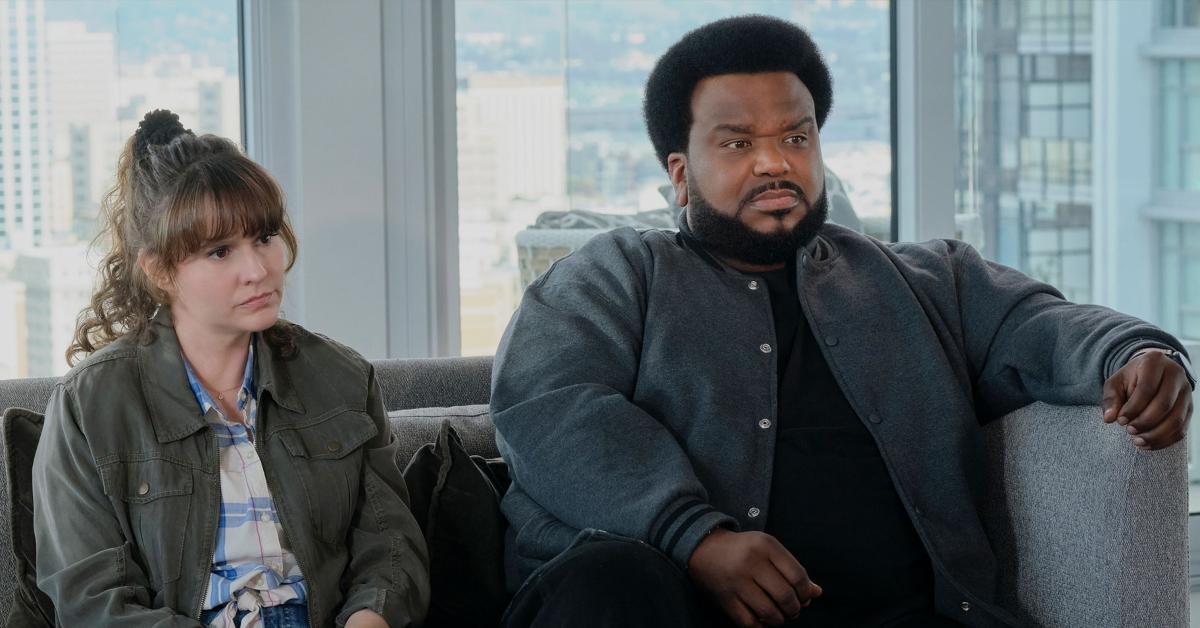 Claudia O'Doherty and Craig Robinson sit on the couch and look concerned in an episode of Peacock's "Killing It". 