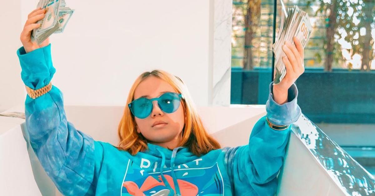 Lil Tay holding money and wearing a bright blue hoodie and sunglasses