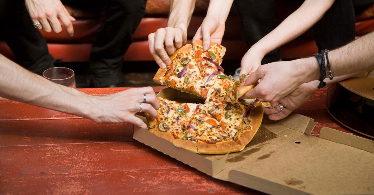 multiple hands reaching for a slice of pizza from the box at the same itme