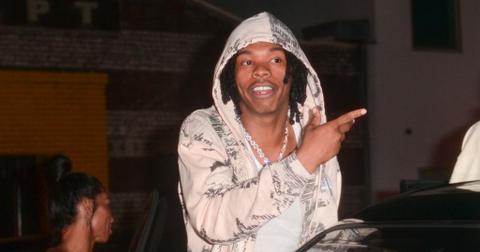 Lil Baby wearring a white hoodie and pointing at something while getting into a car.