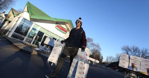 Person carrying donut boxes in front of a Krispy Kreme