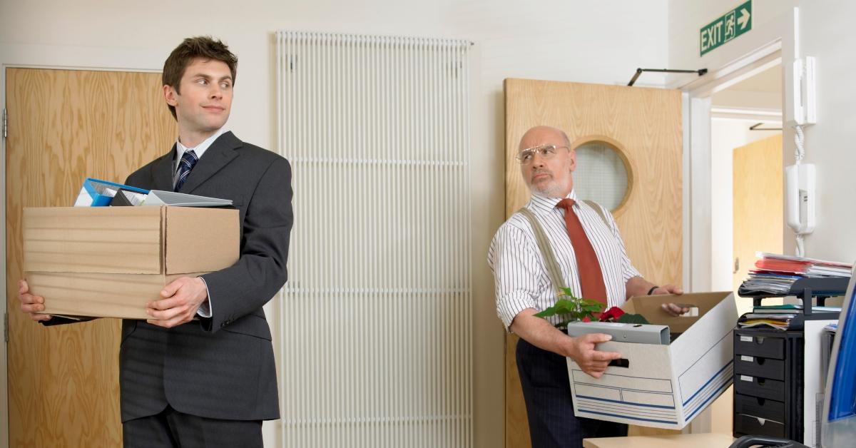 Two men leave an office carrying boxes.