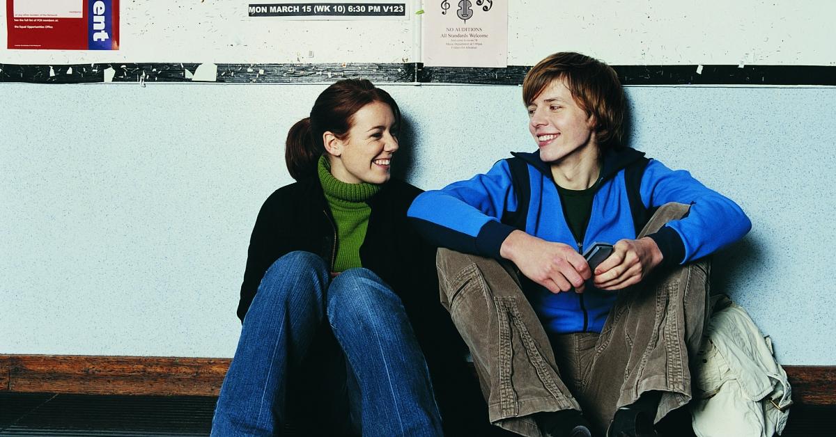 male female college students sitting in a hallway smiling at one another