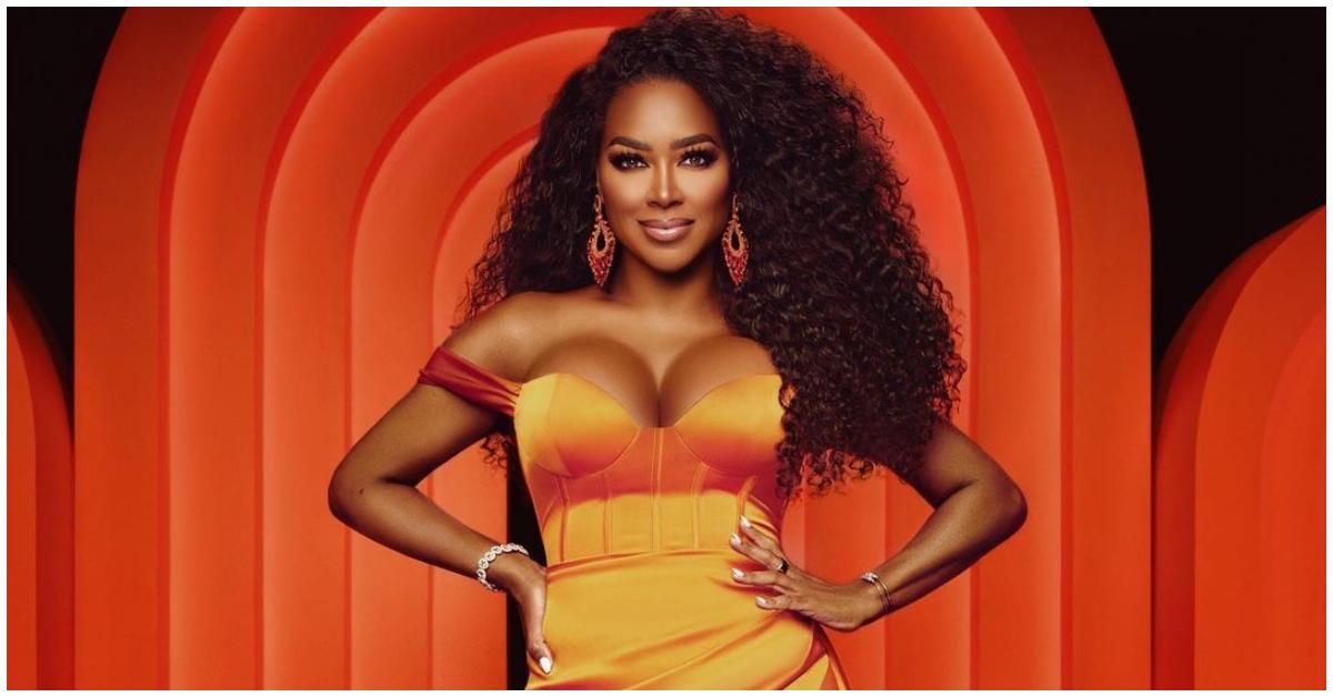 Kenya Moore from 'RHOA' holding her hips in an orange dress.