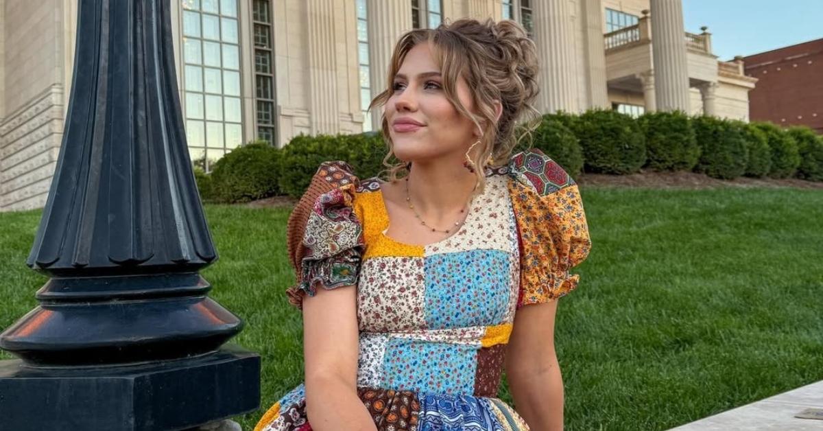 Hannah Harper sits outside on a lawn in a patchwork dress.