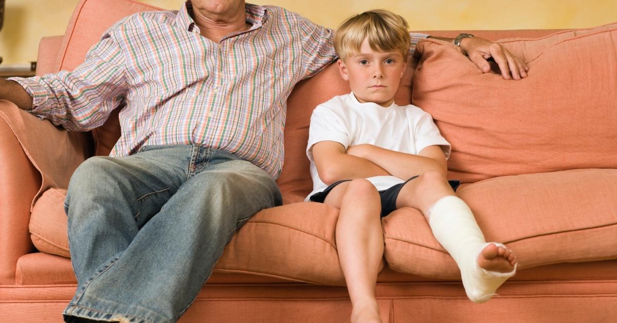 Boy in leg cast sitting with father.